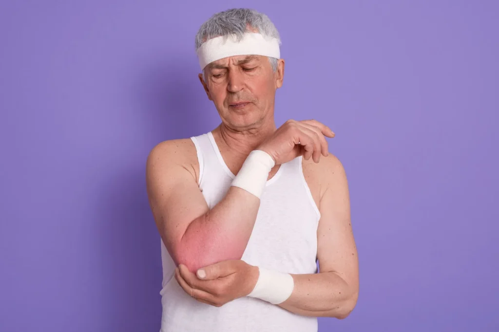 An elderly man wearing white sleeveless t shirt and head band feeling inflammation in his right arm