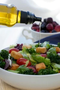 from a bottle olive oil is poring at a bowel of salad