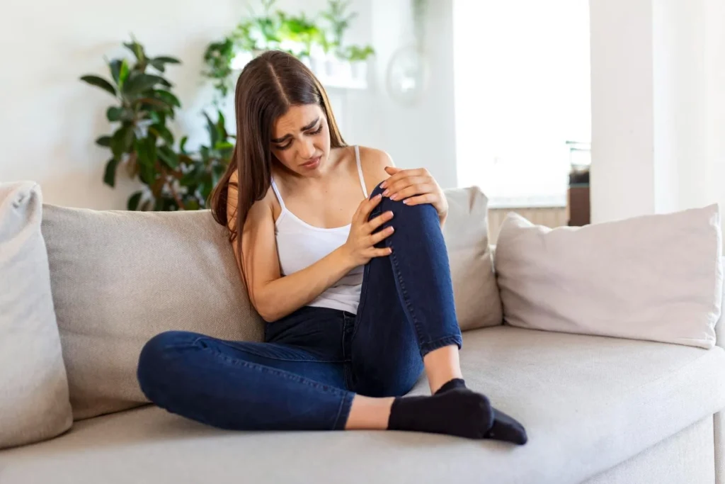 Woman holding the knee with pain on sofa health care and medical concept